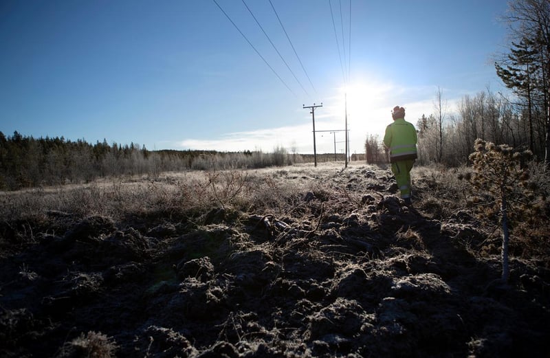Henkilö heijastinvaatteissa kävelee jäisellä polulla, taustalla sähkölinjoja ja metsää.