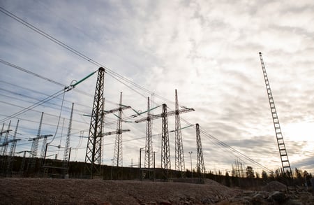 Sähköasema, jossa korkeat teräsrakenteet ja jännitelinjat risteävät vasten pilvistä taivasta