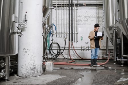 Teollinen ympäristö, putkia ja tankkeja, henkilö lukemassa papereita