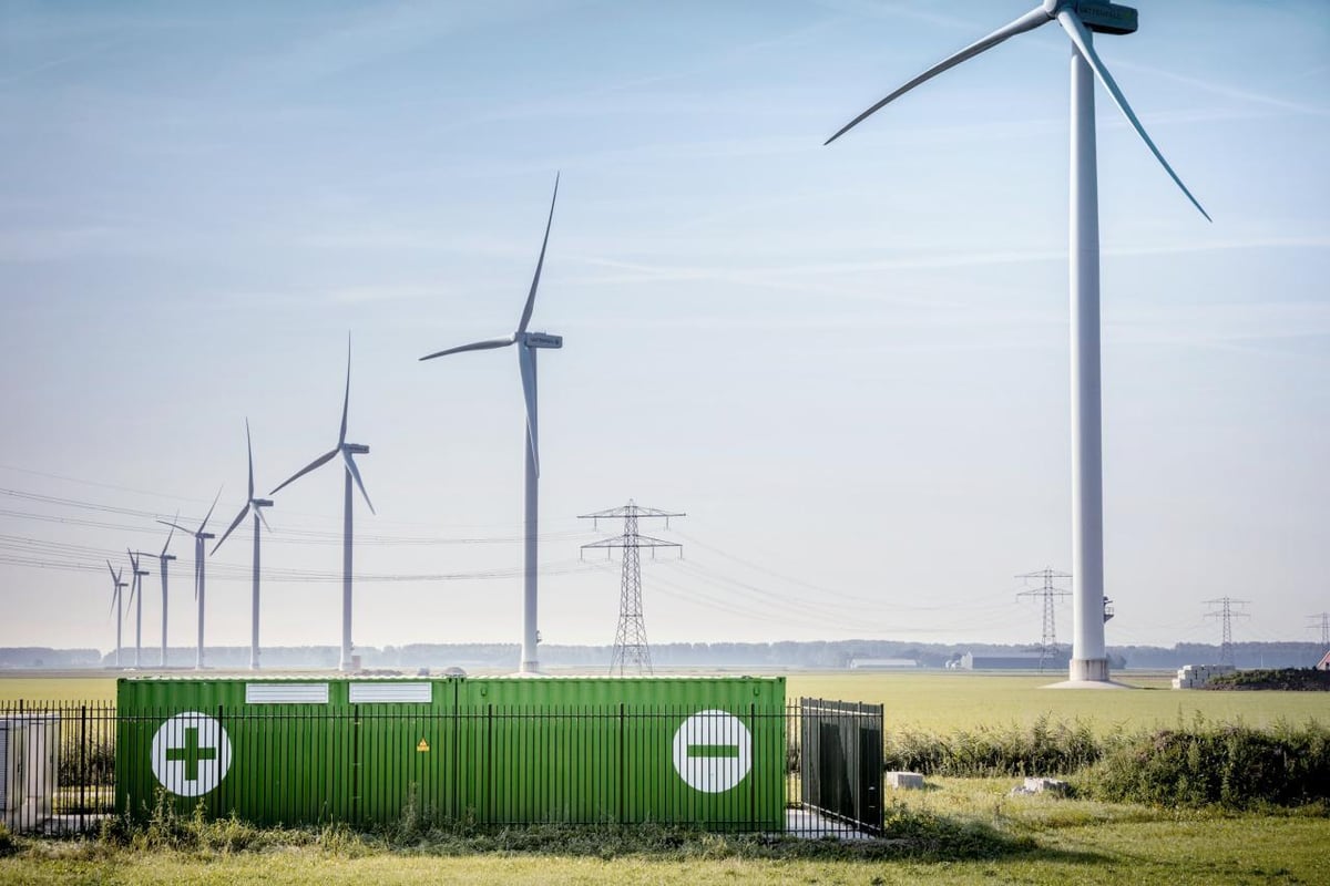 Tuulivoimaloita avoimella peltoalueella. Etualalla energiavarasto, taustalla sähkönsiirtolinjoja.