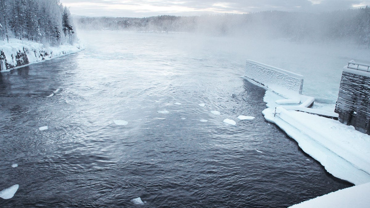 Talvinen joki, jonka ympärillä on lunta ja jäätä sekä oikealla luminen pato